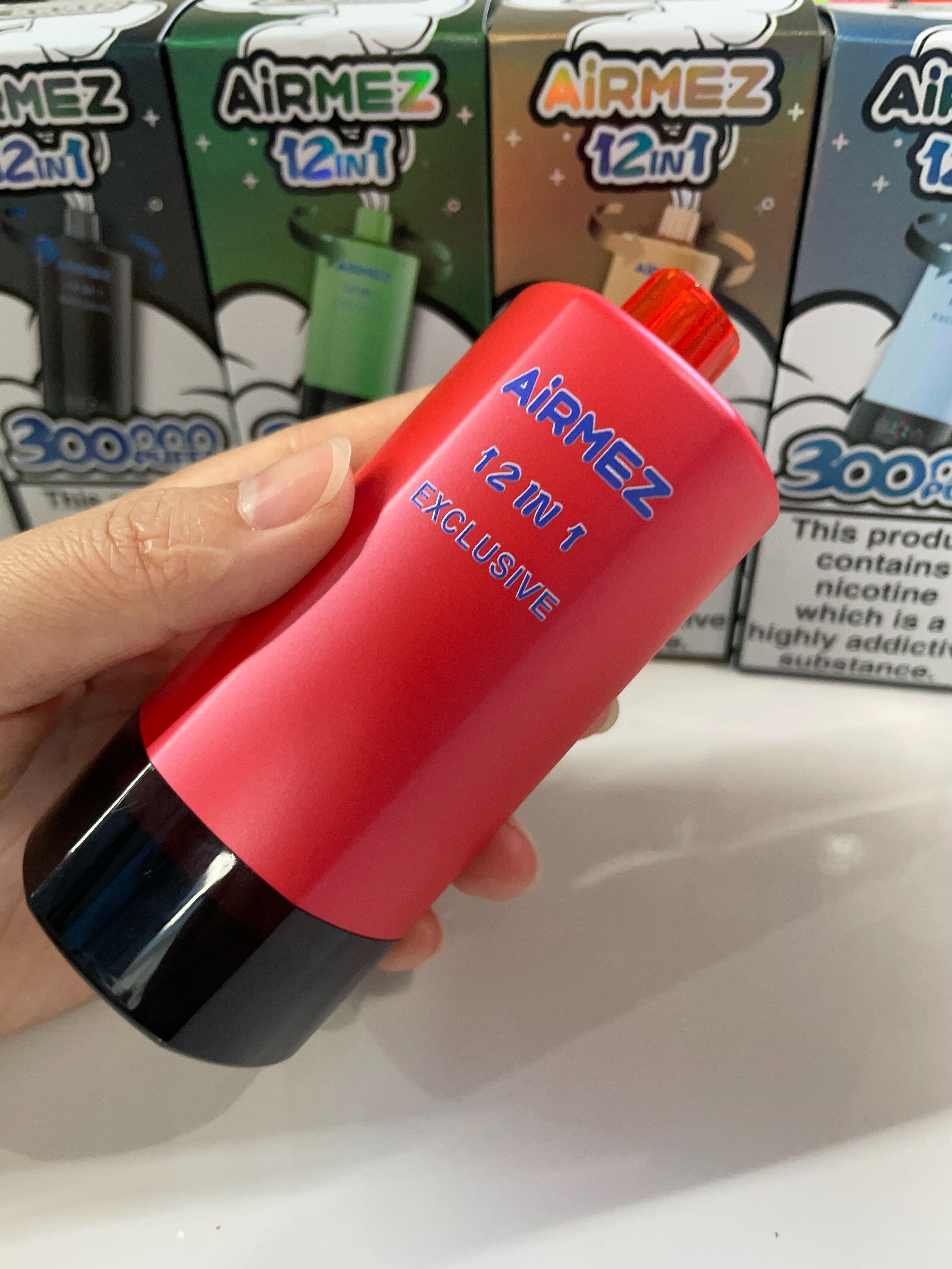 Close-up real photo of red AiRMEZ Exclusive 12-in-1 300K device with retail boxes in background